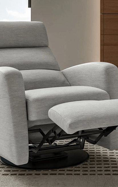 A contemporary light gray recliner with a swivel base is shown in a mid-recline position, revealing its black metal reclining mechanism. It sits on a textured beige rug in a modern room with soft lighting and wood accents.