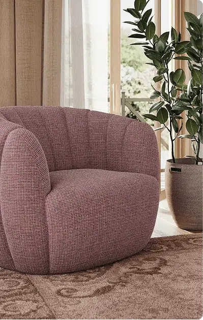 A curved mauve accent chair with subtle vertical tufting sits on a patterned brown rug near tall windows with beige curtains. A large potted plant adds a natural element to the softly lit, elegant space.